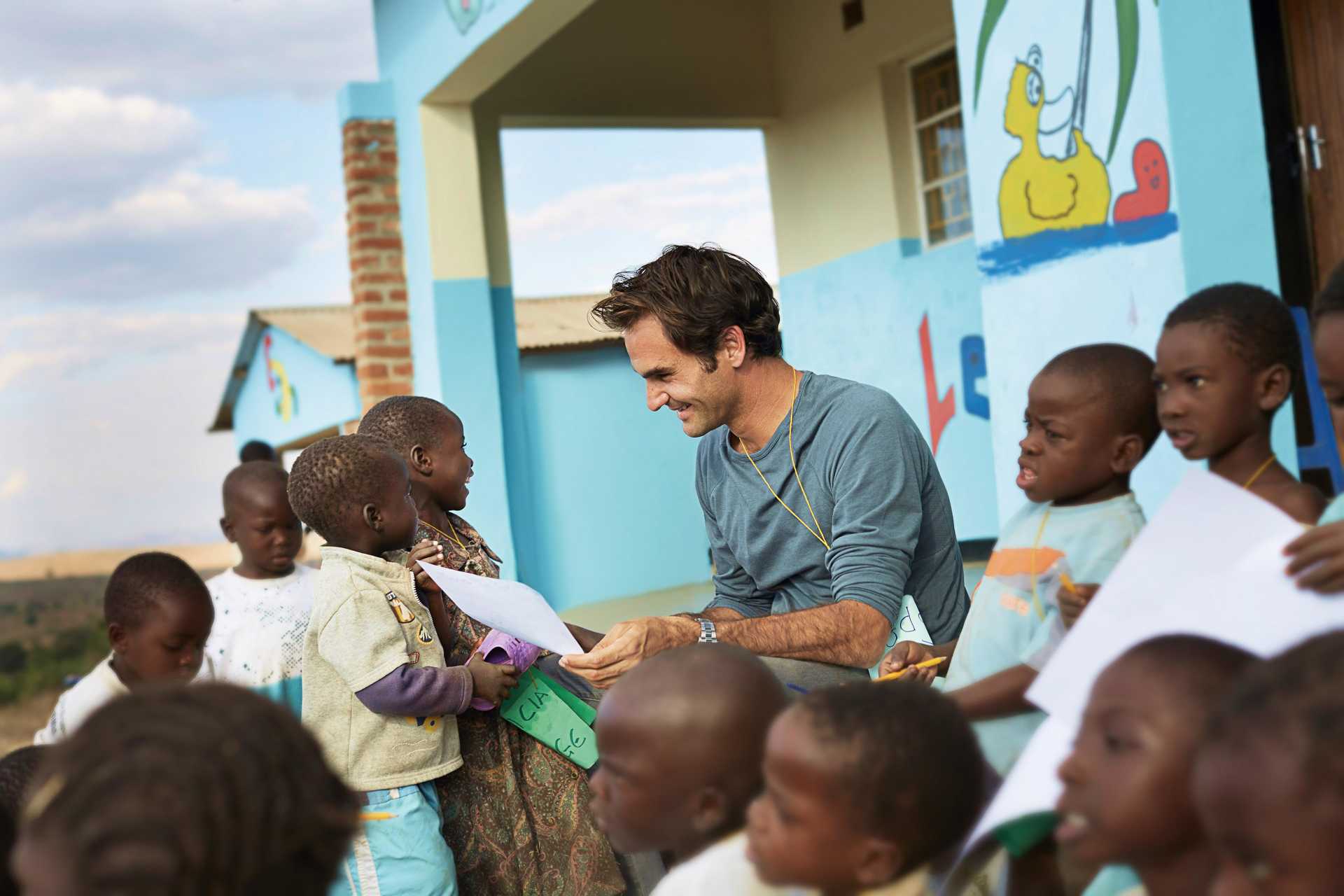 Roger Federer crouching down and smiling as he interacts with young school children